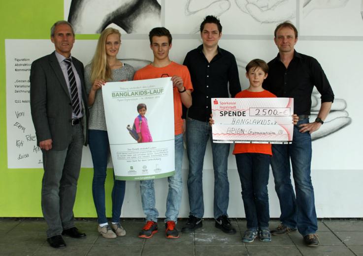 „Freudestrahlend mit dem Bewusstsein etwas Gutes geleistet zu haben, können - stellvertretend für die Schülerinnen und Schüler des Apian-Gymnasiums –  Anabel Knoll (Q 11), Johannes Stahr (9A) und Elias Dirsch (5A), die am 13.10.2013 in 30 Minuten jeweils 7 bzw. 8 Kilometer gelaufen sind, einen Scheck in der Höhe von 2.500.- € an Herrn Mathias Geisenfelder von BANGLAKIDS e.V. überreichen.“